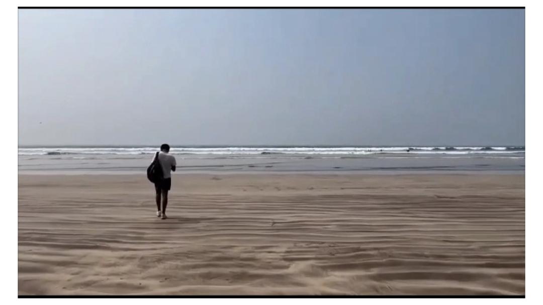 Lone figure crossing a wide empty beach toward a hazy horizon