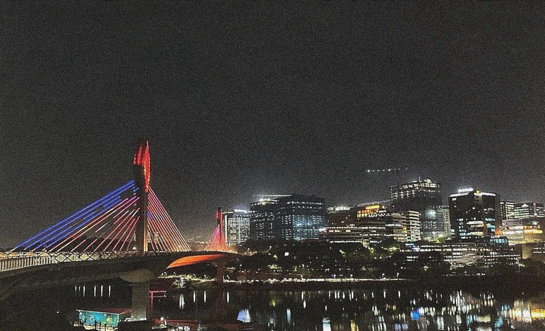 Cable-stayed bridge at night — lit cables, city skyline, river reflections