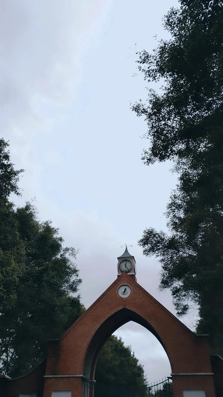 Brick gatehouse — gothic arch and clock tower under an overcast sky