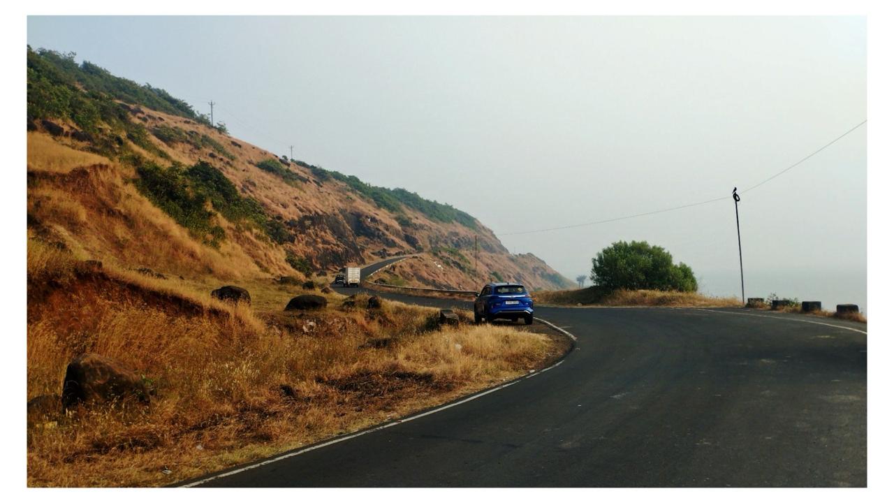 A car on a coastal ghat — winding road along a golden slope